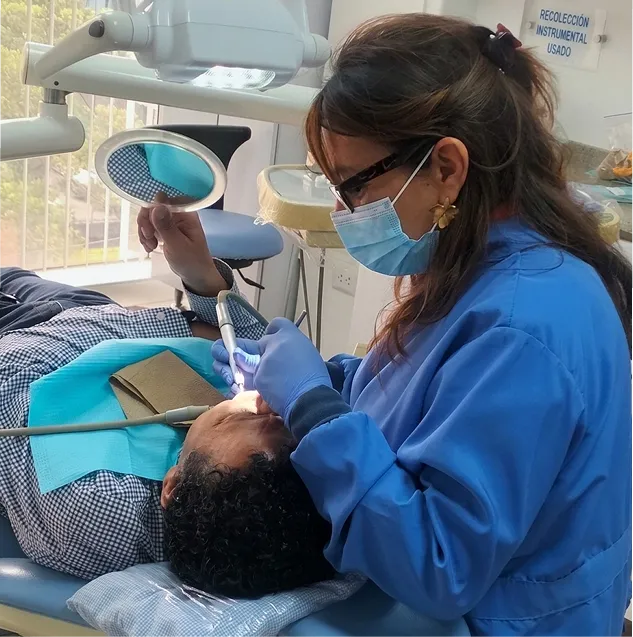 Asistente realizando una limpieza dental con lámpara y espejo